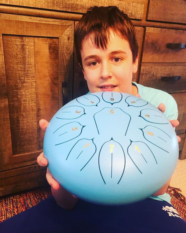 Young Boy Sitting Holding 11 Tone Steel Tongue Hank Tank Panda Drum Blue
