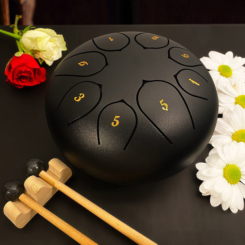 8 Tone 6-inch Steel Tongue Hank Tank Panda Drum Black With Drumsticks on a Table with Flowers