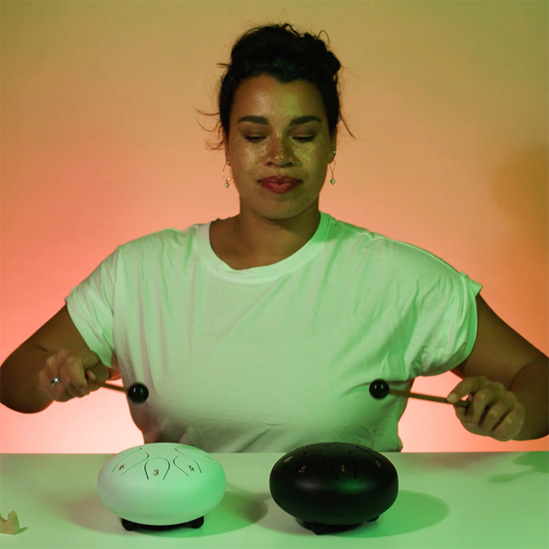 A Woman in White Playing  A 8 Tone 6-inch Steel Tongue Hank Tank Panda Drum White and Black on A White Table