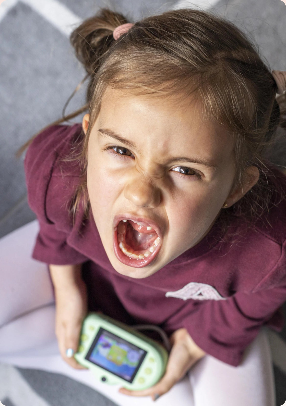 A young child mid-tantrum, clutching a handheld games console